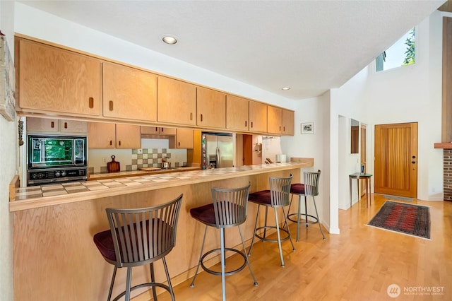 2314 140th Pl SE, Mill Creek, WA 98012 - kitchen featuring built in microwave, stainless steel refrigerator with ice dispenser, black oven, tasteful backsplash, and light wood finished floors