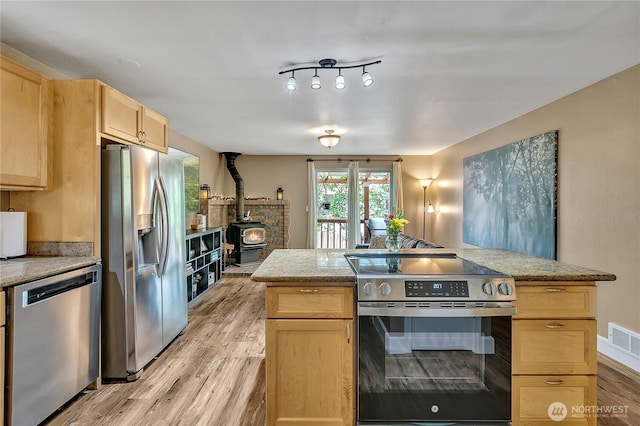 21628 SE 271st St, Maple Valley, WA 98038 - kitchen with stainless steel appliances, light brown cabinets, a wood stove, light wood-style floors, and a center island