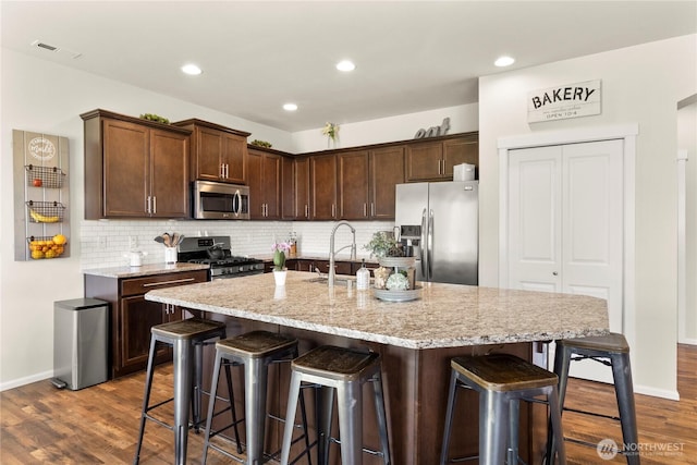 902 Van Ogle Ln NW, Orting, WA 98360 - kitchen with stainless steel appliances, dark wood-style flooring, a breakfast bar, tasteful backsplash, and light stone countertops