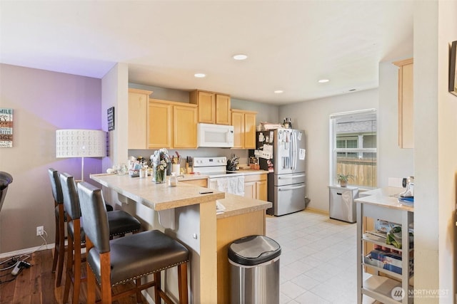 6725 159th St E, Puyallup, WA 98375 - kitchen with white appliances, light brown cabinets, a peninsula, light countertops, and a breakfast bar