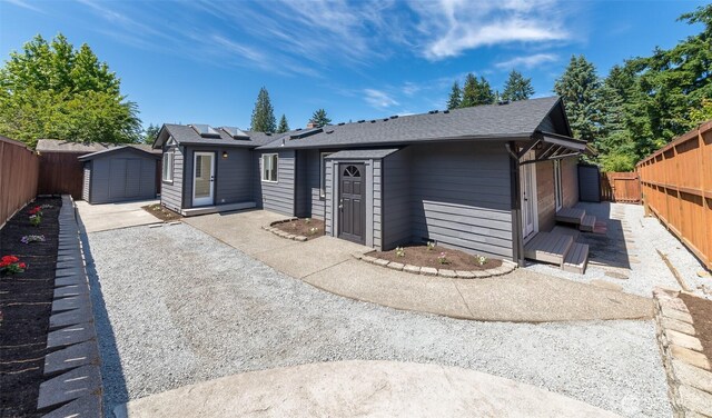 9621 1st Ave SE, Everett, WA 98208 - view of front of house featuring a fenced backyard, a storage unit, roof with shingles, solar panels, and a patio area