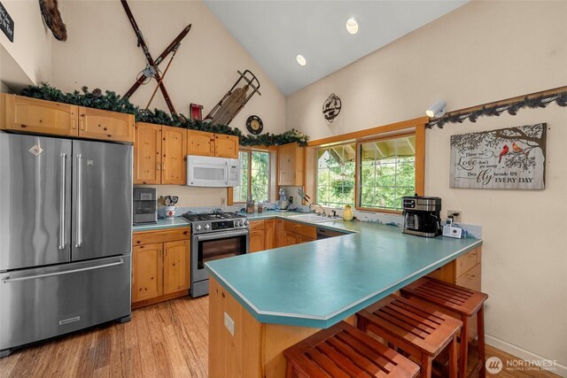 2290 Riffle Dr, Leavenworth, WA 98826 - kitchen featuring appliances with stainless steel finishes, high vaulted ceiling, a peninsula, light wood-type flooring, and a breakfast bar