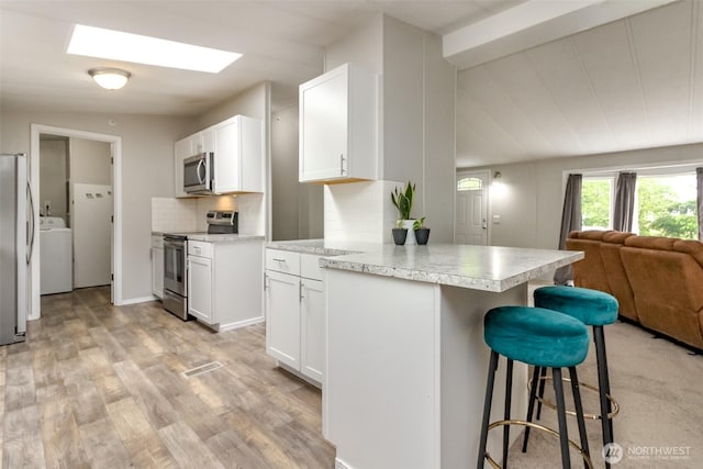 3010 248th Street Ct E, Spanaway, WA 98387 - kitchen featuring appliances with stainless steel finishes, washer / dryer, open floor plan, a kitchen bar, and white cabinets