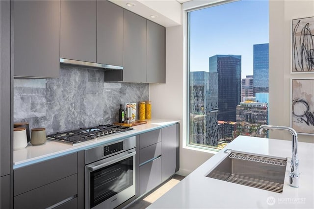 2510 6th Ave Unit 1704, Seattle, WA 98121 - kitchen with appliances with stainless steel finishes, gray cabinets, modern cabinets, decorative backsplash, and under cabinet range hood