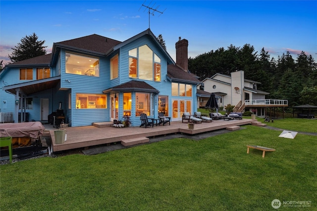 9673 NE Pilot Ct, Kingston, WA 98346 - back of house at dusk featuring a deck, a chimney, a yard, and a shingled roof