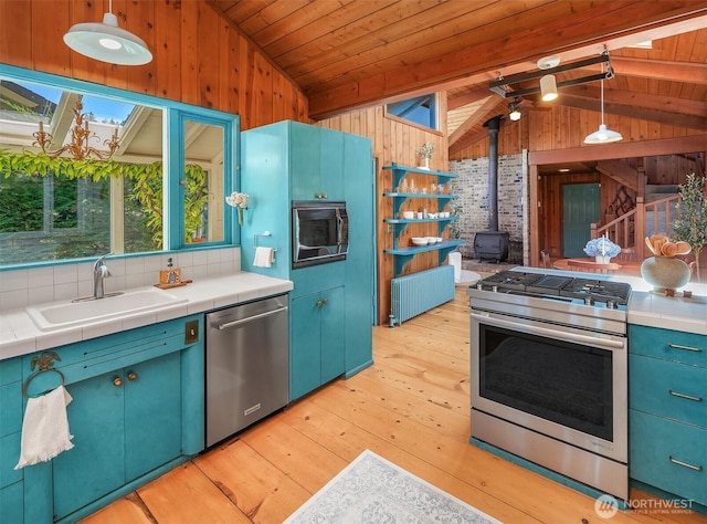 14504 Glen Acres Rd, Vashon, WA 98070 - kitchen with stainless steel appliances, a wood stove, wooden walls, radiator, and light wood finished floors