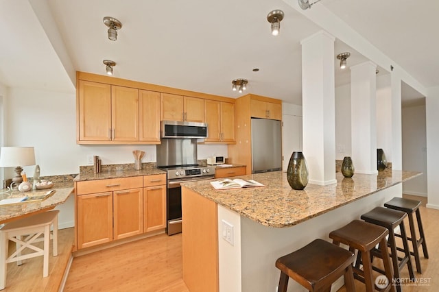 121 Vine St Unit 703, Seattle, WA 98121 - kitchen featuring stainless steel appliances, light stone countertops, a peninsula, a breakfast bar area, and light brown cabinets
