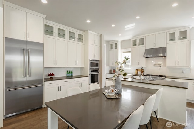 8784 NE Winslow Grove Ct, Bainbridge Island, WA 98110 - kitchen featuring built in appliances, under cabinet range hood, dark countertops, tasteful backsplash, and recessed lighting