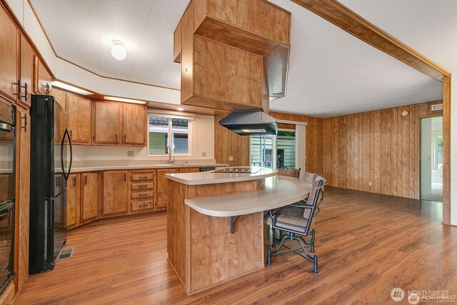 1415 84th St SE Unit 192, Everett, WA 98208 - kitchen with black appliances, light wood-type flooring, light countertops, brown cabinetry, and wooden walls