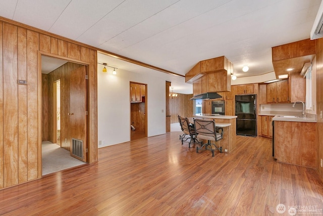 1415 84th St SE Unit 192, Everett, WA 98208 - kitchen featuring black appliances, brown cabinets, wood walls, light countertops, and light wood-style flooring