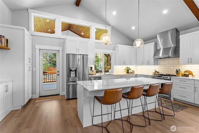 989 Lakewood Ln, Bellingham, WA 98229 - kitchen featuring stainless steel appliances, wall chimney range hood, decorative backsplash, a kitchen bar, and beamed ceiling