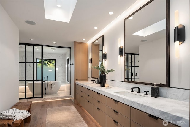 9001 NE 14th St, Clyde Hill, WA 98004 - full bathroom with a skylight, wood finished floors, a freestanding bath, double vanity, and recessed lighting