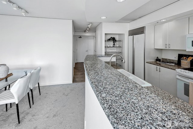 2000 1st Ave Unit 703, Seattle, WA 98121 - kitchen featuring track lighting, white appliances, dark stone countertops, light carpet, and recessed lighting