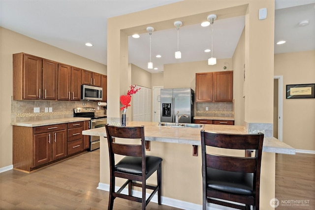 16922 SE 262nd St, Covington, WA 98042 - kitchen featuring appliances with stainless steel finishes, a kitchen bar, decorative backsplash, light wood-style floors, and recessed lighting