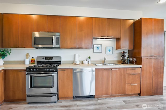 1214 N Northgate Way, Seattle, WA 98133 - kitchen featuring stainless steel appliances, light wood finished floors, brown cabinetry, and tile countertops