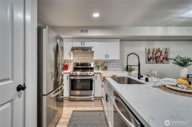 3939 10th St SE Unit C6, Puyallup, WA 98374 - kitchen with stainless steel appliances, under cabinet range hood, white cabinetry, light wood-style floors, and light stone countertops