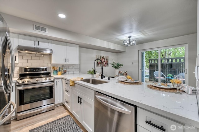 3939 10th St SE Unit C6, Puyallup, WA 98374 - kitchen featuring appliances with stainless steel finishes, under cabinet range hood, white cabinets, light wood-style flooring, and backsplash