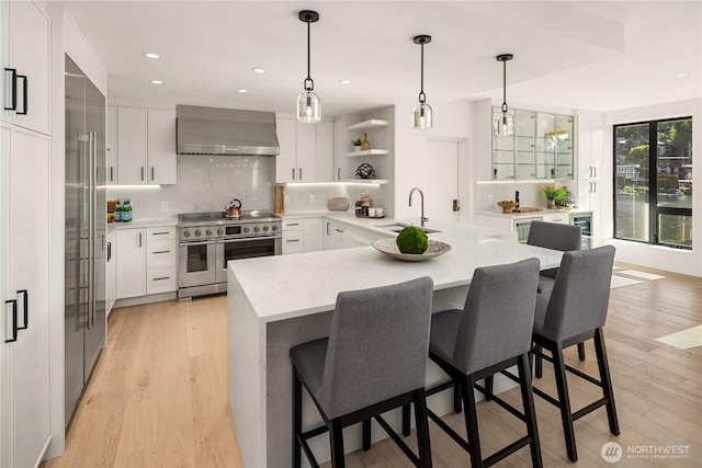 101 101st Ave SE Unit 201A, Bellevue, WA 98004 - kitchen with range with two ovens, wall chimney exhaust hood, a breakfast bar area, white cabinetry, and recessed lighting