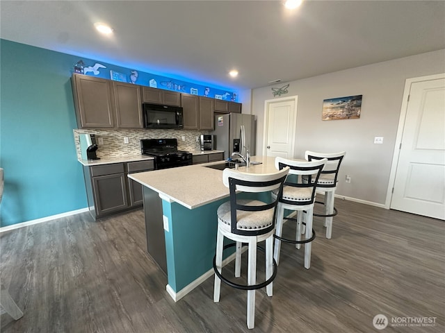 9151 Viola St SE, Tumwater, WA 98501 - kitchen featuring black appliances, dark wood-style flooring, a kitchen island with sink, a kitchen breakfast bar, and light countertops