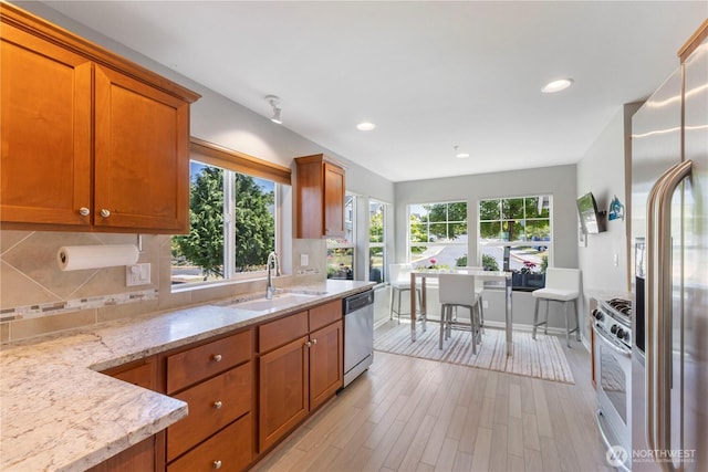 7103 Hazel Pl SE, Auburn, WA 98092 - kitchen featuring stainless steel appliances, brown cabinets, decorative backsplash, light stone countertops, and light wood-style flooring