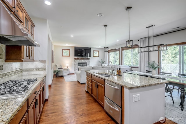 1141 Bell Hill Pl, Dupont, WA 98327 - kitchen featuring under cabinet range hood, appliances with stainless steel finishes, brown cabinetry, a glass covered fireplace, and light wood finished floors