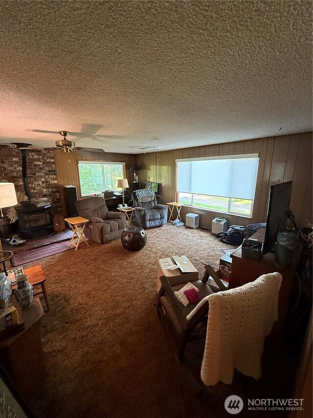 5645 Lento Pl SE, Olympia, WA 98513 - living room featuring a wood stove, a textured ceiling, carpet floors, wood walls, and a ceiling fan