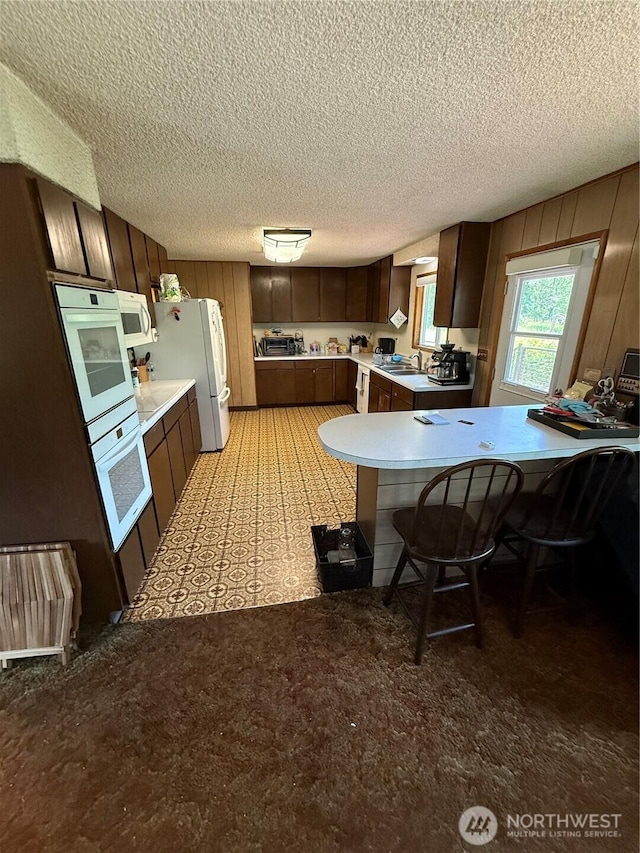 5645 Lento Pl SE, Olympia, WA 98513 - kitchen with white appliances, light countertops, a textured ceiling, dark brown cabinetry, and a peninsula
