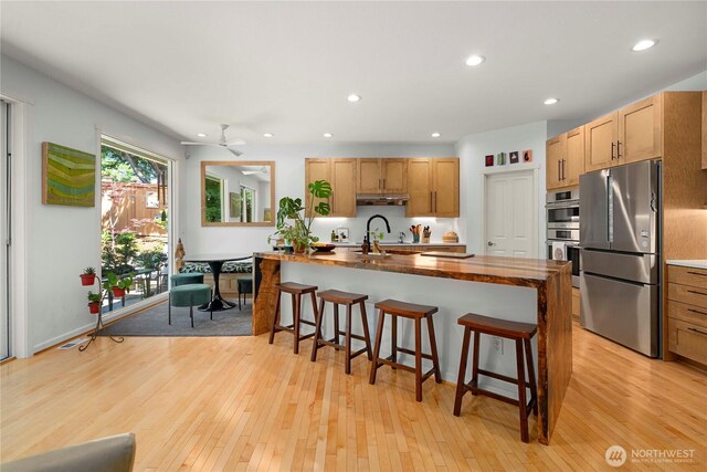 6703 Marshall Ave SE, Auburn, WA 98092 - kitchen featuring stainless steel appliances, a breakfast bar, light wood-style flooring, recessed lighting, and an island with sink