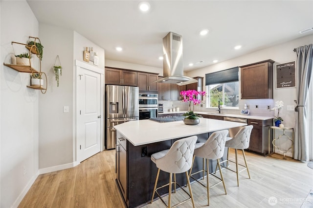 18437 111th Ave E, Puyallup, WA 98374 - kitchen featuring appliances with stainless steel finishes, island range hood, backsplash, a breakfast bar area, and light wood-type flooring