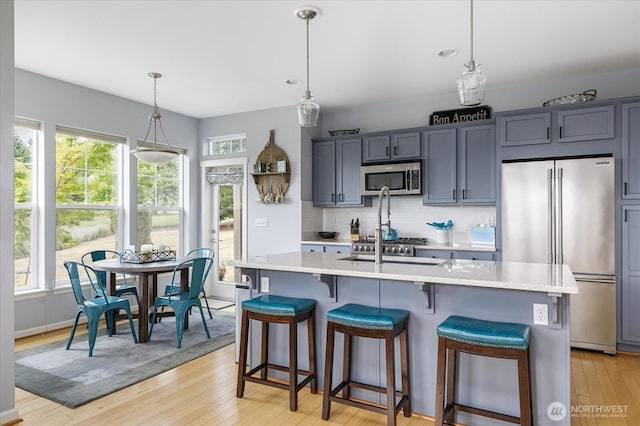 1404 Portside Ct, Freeland, WA 98249 - kitchen featuring stainless steel appliances, light countertops, light wood finished floors, a breakfast bar, and an island with sink