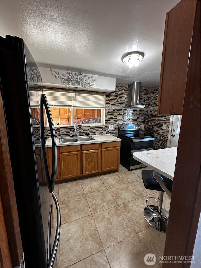 438 Biggs Dr, Moses Lake, WA 98837 - kitchen with stainless steel range with electric cooktop, wall chimney range hood, fridge, light countertops, and brown cabinetry