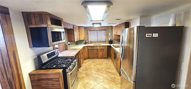 20354 Adrian Rd NE, Soap Lake, WA 98851 - kitchen with stainless steel appliances, light countertops, brown cabinetry, a textured ceiling, and light tile patterned flooring