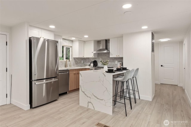 15409 Westshore Dr SE, Yelm, WA 98597 - kitchen with appliances with stainless steel finishes, wall chimney range hood, light wood-type flooring, a breakfast bar area, and white cabinetry
