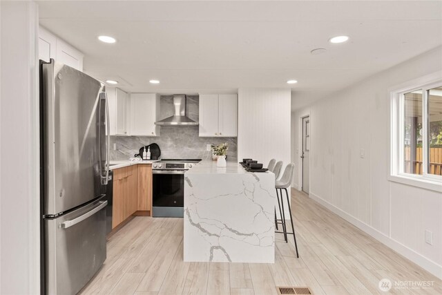 15409 Westshore Dr SE, Yelm, WA 98597 - kitchen featuring appliances with stainless steel finishes, wall chimney exhaust hood, light wood finished floors, a kitchen breakfast bar, and light stone countertops