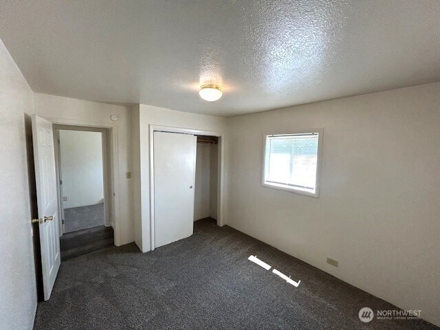1004 8th, Longview, WA 98632 - unfurnished bedroom featuring dark colored carpet, a closet, and a textured ceiling