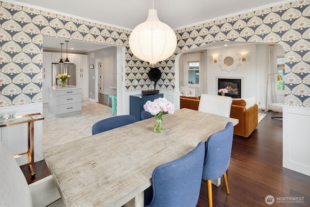 3249 27th Ave W, Seattle, WA 98199 - dining space with wallpapered walls, crown molding, a fireplace, light wood-style floors, and arched walkways