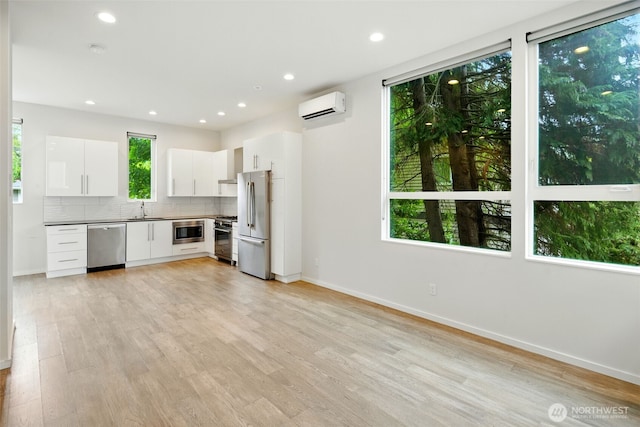9732 Woodlawn Ave N Unit A, Seattle, WA 98103 - kitchen with appliances with stainless steel finishes, a wall mounted air conditioner, backsplash, white cabinetry, and light wood-style floors