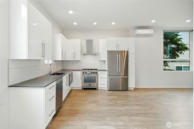 9732 Woodlawn Ave N Unit A, Seattle, WA 98103 - kitchen with stainless steel appliances, wall chimney exhaust hood, an AC wall unit, dark countertops, and light wood-style flooring