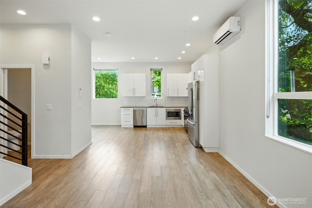 9732 Woodlawn Ave N Unit A, Seattle, WA 98103 - kitchen with a wall mounted AC, appliances with stainless steel finishes, light wood-style floors, white cabinets, and backsplash