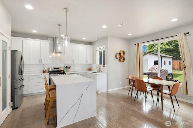 8438 Tacoma Ave S, Tacoma, WA 98444 - kitchen featuring wall chimney range hood, appliances with stainless steel finishes, tasteful backsplash, a center island, and light wood-style floors