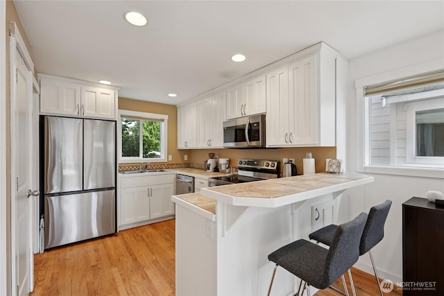 8450 25th Ave SW Unit B, Seattle, WA 98106 - kitchen with stainless steel appliances, a kitchen bar, a peninsula, white cabinetry, and light wood-style flooring