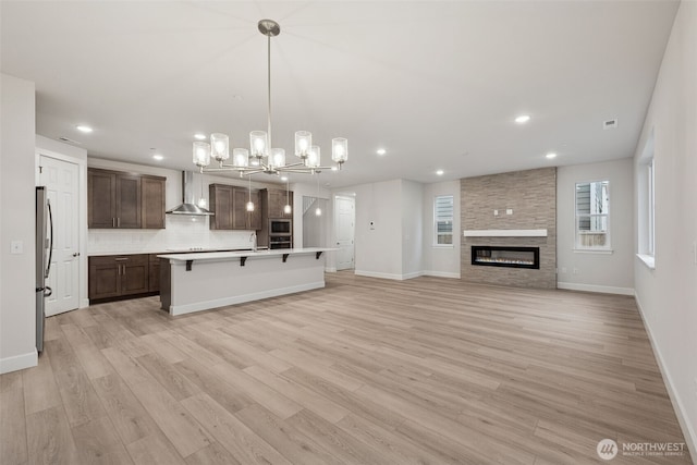 20424 E 97th Ave E Unit 6, Graham, WA 98338 - kitchen featuring wall chimney exhaust hood, stainless steel appliances, a chandelier, dark brown cabinets, and light wood-type flooring