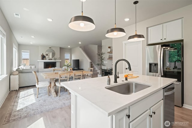 2405 NE Waterlily Way, Poulsbo, WA 98370 - kitchen featuring light wood finished floors, a warm lit fireplace, decorative light fixtures, white cabinetry, and light stone counters