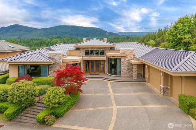 7215 Saint Andrews Ln SE, Snoqualmie, WA 98065 - view of front facade featuring a standing seam roof, stone siding, a mountain view, a metal roof, and a chimney