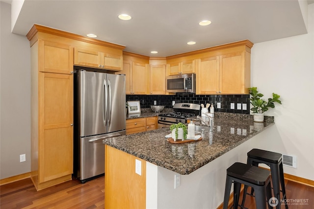 10290 NE Ruddy Duck Ln, Bainbridge Island, WA 98110 - kitchen featuring stainless steel appliances, light brown cabinetry, wood finished floors, a peninsula, and decorative backsplash
