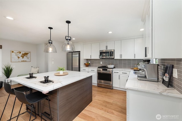 18114 NE 23rd St, Redmond, WA 98052 - kitchen featuring appliances with stainless steel finishes, a breakfast bar area, decorative backsplash, white cabinets, and light wood-type flooring
