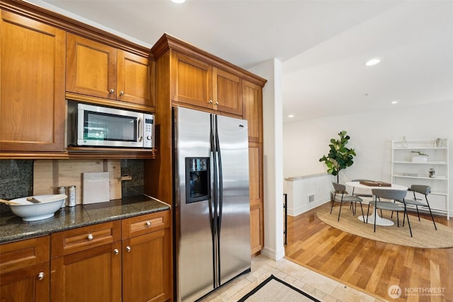 2551 Thorndyke Ave W Unit 203, Seattle, WA 98199 - kitchen with appliances with stainless steel finishes, brown cabinetry, backsplash, dark stone counters, and recessed lighting