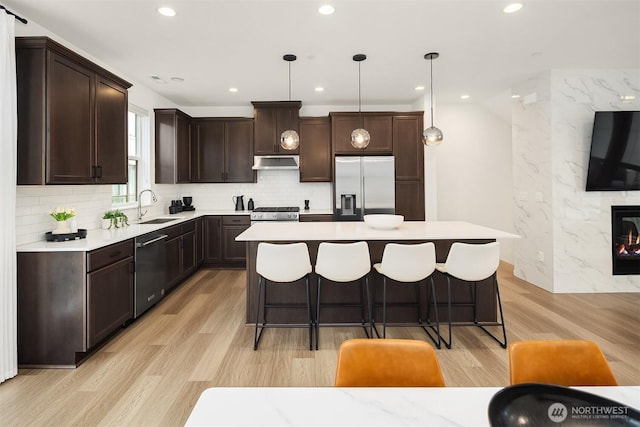 21822 25th Ave SE Unit B, Bothell, WA 98021 - kitchen featuring stainless steel appliances, under cabinet range hood, dark brown cabinetry, a kitchen island, and light wood finished floors