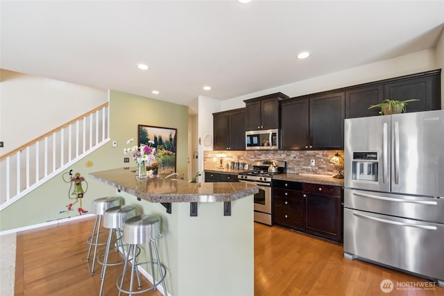 26707 NE 144th Ct, Duvall, WA 98019 - kitchen with stainless steel appliances, light wood-type flooring, a kitchen breakfast bar, tasteful backsplash, and an island with sink