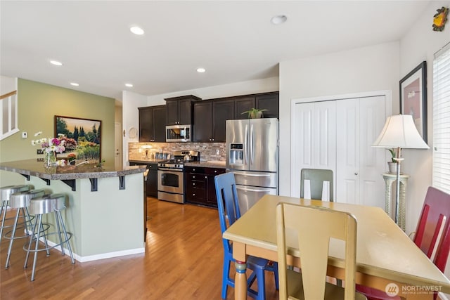 26707 NE 144th Ct, Duvall, WA 98019 - kitchen with appliances with stainless steel finishes, light wood finished floors, a kitchen bar, tasteful backsplash, and dark brown cabinets